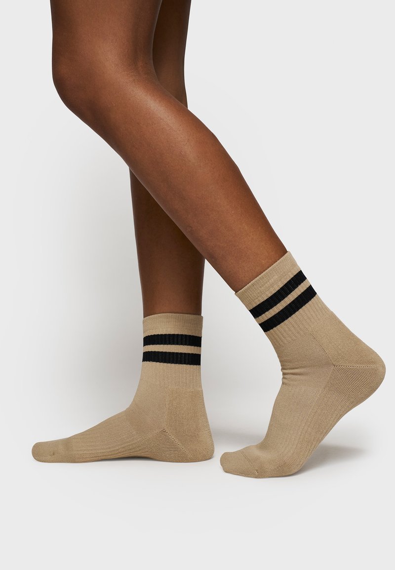 Beige bomuldsstrømper med sorte vandrette striber, mellemlang længde, ribbet tekstur, forstærket tå og hæl for holdbarhed.