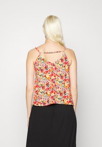 Top de alças finas com estampado floral, apresentando uma mistura vibrante de flores vermelhas, laranjas e amarelas sobre um fundo claro. A parte de trás tem um detalhe recortado.