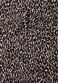 Tissu à imprimé léopard noir et crème présentant un motif texturé avec des formes irrégulières et des surfaces lisses partout.