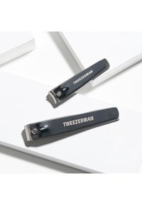 Due tagliaunghie in metallo nero etichettati "TWEEZERMAN" posizionati su superfici geometriche bianche.