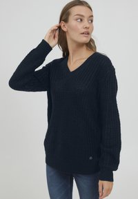 Maglione a V in navy scuro con un design chunky a maglia testurizzata, caratterizzato da maniche morbide e un orlo a coste.