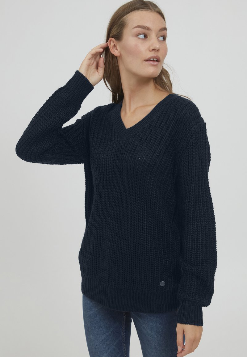 Maglione a V in navy scuro con un design chunky a maglia testurizzata, caratterizzato da maniche morbide e un orlo a coste.