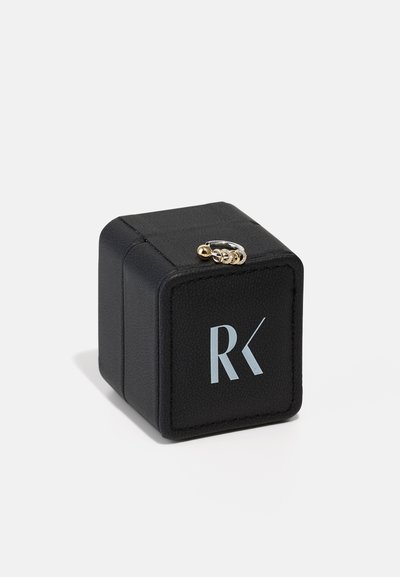 Svart konstläder ringlåda med präglad logotyp "RK" i ljusblått. Fyrkantig form, med guldfärgad detalj på toppen. Sido vy visas.