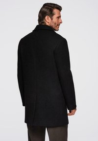 Svart ullkapp med en strukturerad design, framträdande krage och rak sk�ärning. Har en dubbelsprund bak och en mjuk textur.