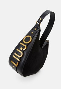Schwarze Handtasche aus Leder und Wildleder, mit einem Logo und Hardware in Goldtönen, kurvenförmigem Design und verstellbarem Tragegurt.