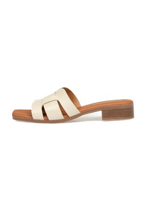 Sandalias deslizantes de cuero beige con múltiples correas recortadas y un tacón cuadrado marrón. Textura suave con un ligero brillo en la parte superior.