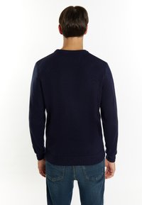 Maglione lavorato a maglia blu navy con un collo a giro, maniche lunghe e polsini a coste, mostrato da dietro. La texture appare liscia ed uniforme.