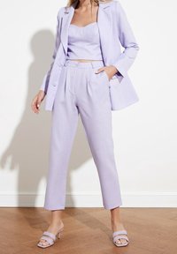 Licht lila twee-delig pak met een getailleerde blazer en een aansluitend crop top. De stof heeft een soepele textuur; de broek is recht afgesneden met een knoopdetail.