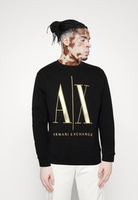 Sort sweatshirt med guld "AX" logo og teksten "ARMANI EXCHANGE". Lange ærmer og ribbede manchetter. Glat stofstruktur.