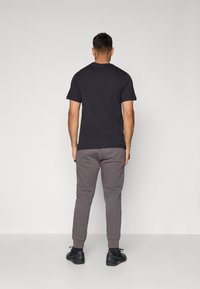 Schwarzes Baumwoll-T-Shirt mit kurzen Ärmeln, kombiniert mit grauen Jogginghosen mit gerippten Bündchen und schwarzen Sportschuhen.