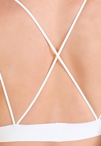 Λευκό βρακάκι με σχέδιο σταυροειδούς ζώνης στην πλάτη, φτιαγμένο από λεία ύφασμα με φαρδιά στήριξη για στήριξη.