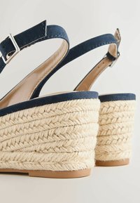 Sleehakken met marineblauwe bandjes en gespen, met dikke, gevlochten zolen van natuurlijke vezels en beige binnenzolen.