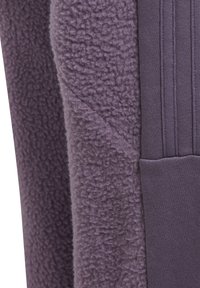 Lila fleecejacka med en strukturerad utsida och släta sidpaneler, med en framficka och ribbade detaljer på sidorna.