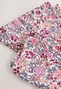 Blommigt tyg i vitt med rosa, röda och blå blommor. Materialet har en mjuk struktur med fransiga kanter och detaljerad design.