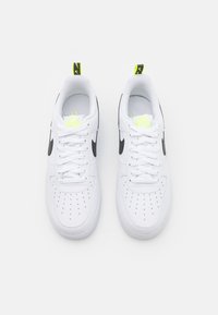 Vita lädersneakers med svart Nike-logga, perforerat tådesign, gula accenter på tungan och hälen samt vita snörning.