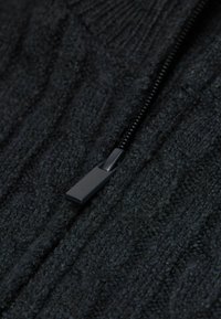Gros plan sur un pull en tricot noir, présentant un tissu texturé avec un zip de couleur sombre contrastante.