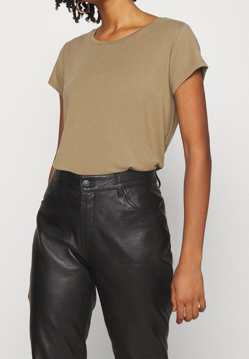 T-shirt à manches courtes vert olive en tissu léger, associé à un pantalon en cuir noir taille haute avec une finition brillante et des poches avant.