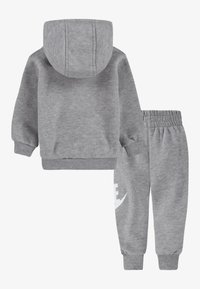 Conjunto de hoodie cinza e calças de fato feitas de tecido macio. Apresenta um capuz, punhos canelados e uma cintura elástica. Logótipo branco notável nos calções.