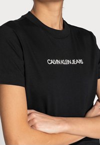 T-shirt in cotone nero con maniche corte e scollatura a girocollo. Sul davanti è stampato "CALVIN KLEIN JEANS" in lettere bianche.