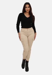 Sort ribbet langærmet top kombineret med beige cargobukser med lynlåslommer og tætsiddende manchetter, båret med sorte ankelstøvler.