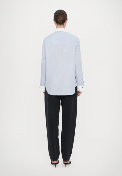 Light blue striped shirt with a white collar, long sleeves, and buttoned cuffs, paired with dark, wide-leg trousers. Minimalist design.