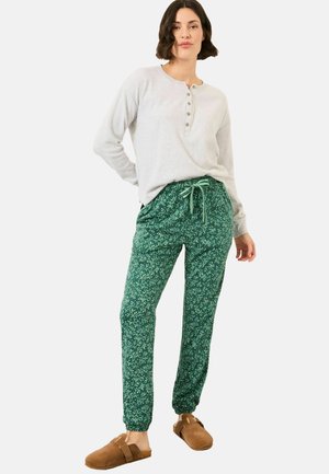 Light gray long-sleeve henley top with button details, paired with green patterned jogger pants and brown slip-on footwear.