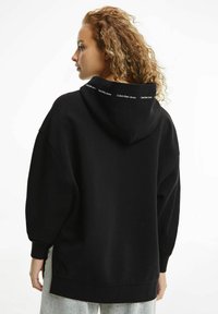 Felpa nera con vestibilità rilassata, dotata di cappuccio e logo Calvin Klein Jeans lungo il colletto. Tessuto morbido con una texture liscia.