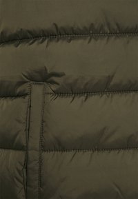 Chaqueta acolchada verde oliva con textura suave y brillante, que presenta costuras horizontales, una cremallera oculta y una lengüeta para cierre.