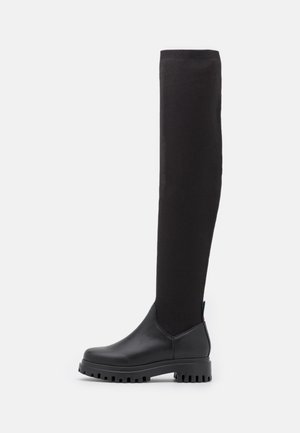 Bottes noires montant jusqu'aux genoux avec une partie inférieure en cuir lisse et une tige en tricot côtelé. La semelle épaisse présente un profil texturé pour une meilleure adhérence.