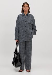 Zwart-wit gestreepte oversized blouse met knopen, een borstzak, bijpassende wijde broek en een zwarte glanzende handtas.