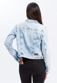 Jasnoniebieska kurtka dżinsowa z wyblakłym wykończeniem, z rękawami do pełnej długości, zapięciem na guziki przy mankietach oraz krótkim krojem. Posiada tylne kieszenie oraz naszywkę z logo.