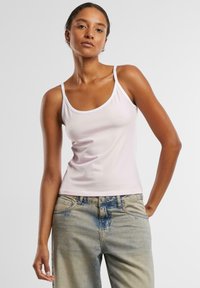Lys rosa ermeløs tank topp med rund halsringning og hvit kant, kombinert med falmede blå jeans. Stoffet virker glatt og elastisk.
