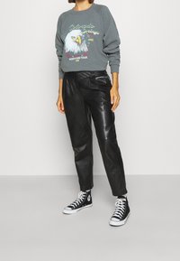 Šedá mikina s grafikou orla, kombinovaná s černými koženými kalhotami a černými kotníkovými teniskami. Neformální styl s kontrastními materiály.