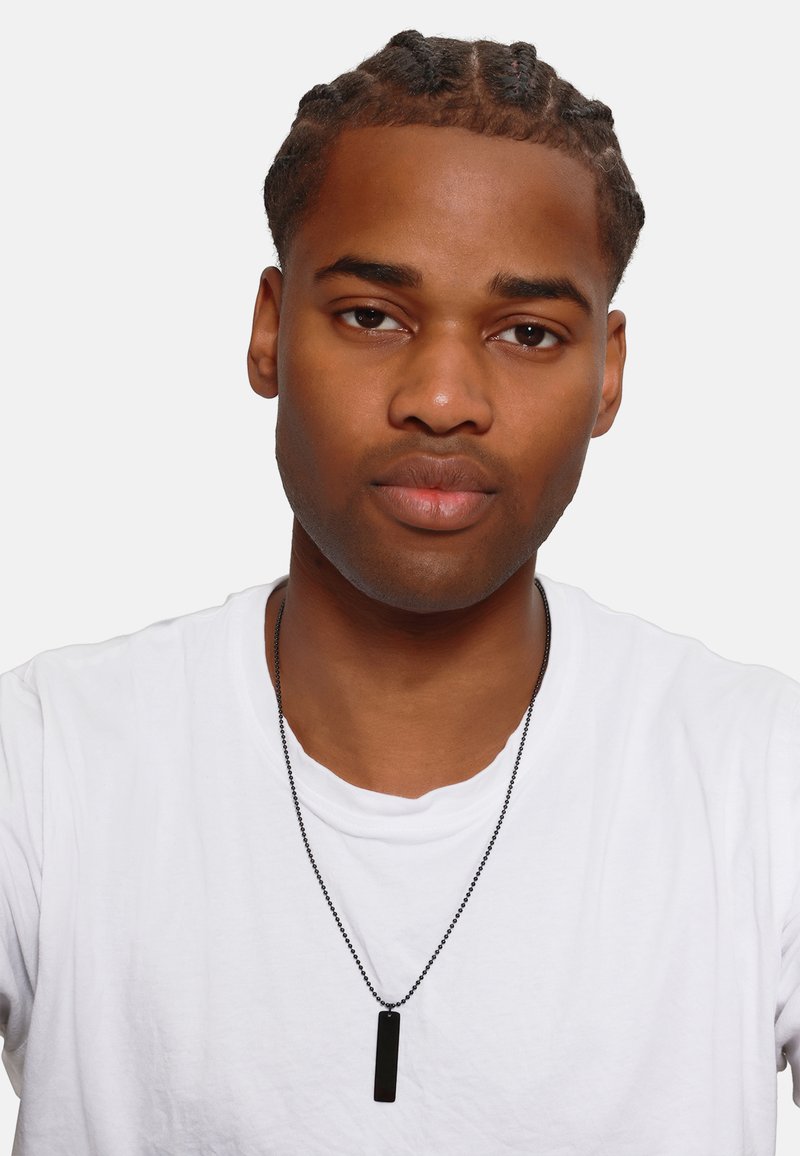Zwart rechthoekig hanger kettingpendant op een zwarte ketting, gedragen over een wit t-shirt. De hanger heeft een gladde, glanzende textuur.