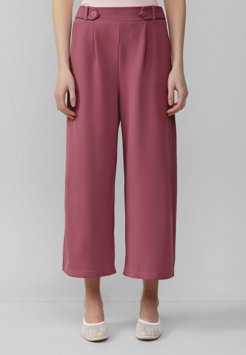 Pantalons à jambes larges dans une teinte rose, en tissu lisse avec un léger éclat, plis sur le devant et deux boutons décoratifs à la taille.