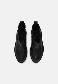 Musta nahkakengät nilkkamallia, joissa on pyöreät varpaat, joustavat sivupaneelit ja vetolenkit. Teksturoitu kumipohja, jossa on yksityiskohtainen ommel.