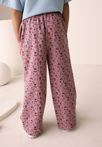Pantaloni a gamba larga con motivo floreale rosa, dotati di una fascia elastica in vita, realizzati in tessuto morbido e decorati con piccoli fiori rossi e blu su tutta la superficie.