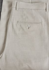 Beige patterned trousers with a subtle checked design, featuring a back pocket with a button closure and belt loops. Made from woven fabric.