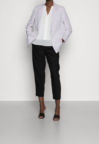 Blazer violet clair avec un design ajusté, haut à col blanc et pantalon cropped noir. Chaussures à enfiler ouvertes noires. Textures lisses.