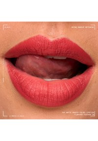 Gros plan sur des lèvres avec un rouge à lèvres mat corail-rose, la langue touche légèrement la lèvre supérieure, montrant une texture lisse et des détails naturels de la peau.