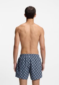 Calções de banho azuis com padrão de grade e texto "HUGO", cintura elástica e corte largo, apresentados de costas.