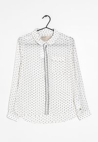 Biała przezroczysta koszula z guzikami z czarnym kwiatowym wzorem, spiczastym kołnierzykiem, przednią kieszonką i czarnym obszyciem wzdłuż listwy guzikowej oraz rękawów.