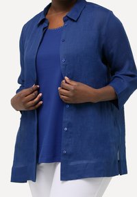 Marinblå, lätt knäppt skjorta med trekvartslånga ärmar, med rak passform och subtil textur. Bärs ovanpå en matchande topp.