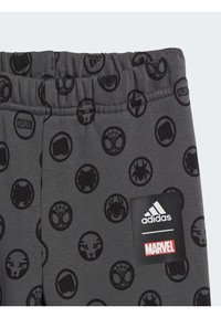 Pantaloni sportivi grigi con loghi di personaggi Marvel neri disposti in motivi circolari e un'etichetta con il logo Adidas sulla vita. Materiale morbido, vita elastica.