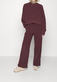 Mörk röd fleece-sweatshirt med kortad design och svart Nike-logotyp; matchande lösa mörkröda byxor; beige sneakers med mönstrade detaljer.