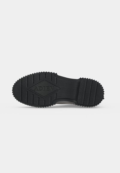 Semelle de chaussure en caoutchouc noir avec motif de grip texturé et "ADIEV" embossé au centre, présentée sur fond blanc uni.