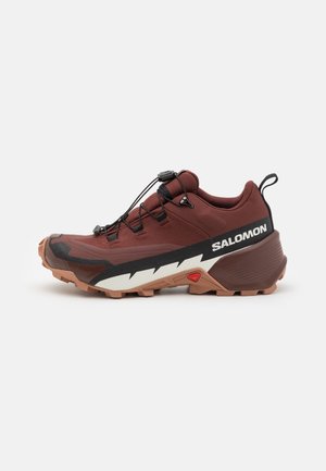 Chaussure de trail de course bordeaux avec tissu texturé, accents noirs et une semelle extérieure blanche dotée de crampons proéminents pour la traction. Lacets à réglage par toggle.