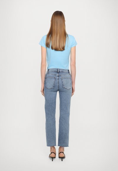 Hellblaues kurzärmeliges Hemd, kombiniert mit hellblauen Jeans. Die Jeans haben einen geraden Schnitt und sichtbare Gesäßtaschen, mit ausgefransten Säumen.