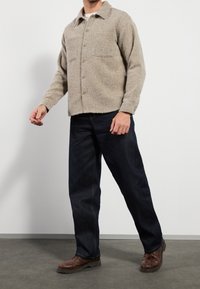 Kurtka z teksturowanym wykończeniem i zapięciem na guziki, z dwoma przednimi kieszeniami, zestawiona z ciemnoniebieskimi dżinsami i brązowym obuwiem. Prosty fason i luźny krój.