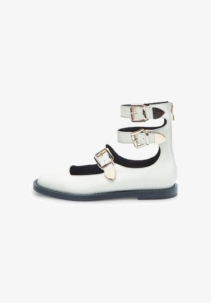 Baltos odinės bateliai su kulkšnies dirželiu, trimis reguliuojamais sagtukais, smailiu pirštu ir plokščiu juodu padu. Iškirpti raštai šoninėse dalyse.